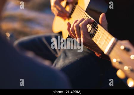 Mid section of caucasian man playing guitar on the beach at sundown Stock Photo