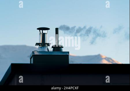 Close up of smoking iron pipe chimney with snow mountain background, Austria Stock Photo