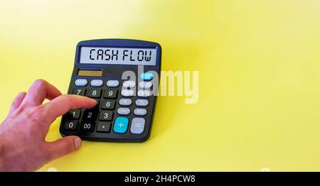 Cash flow on the display of the calculator on a yellow background. Male hand on a calculator Stock Photo