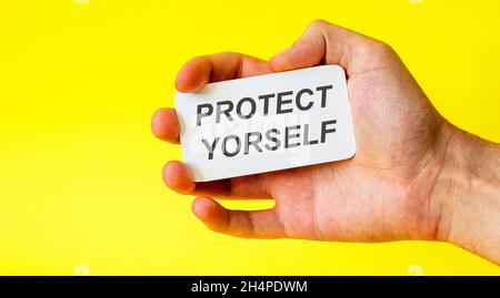 Businessman holds a card with the text protect yourself on a yellow background Stock Photo
