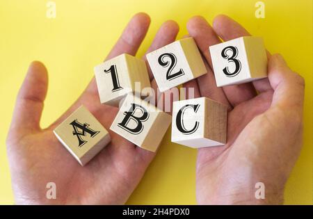 Hands holding cubes on a yellow background with the text 1 2 3 A B C Stock Photo