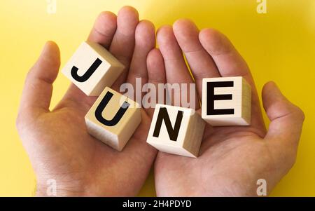 Men's hands are holding wooden blocks with the text June on a yellow background Stock Photo