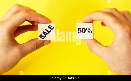 Man holds cubes with the text sale and 50 on a yellow background Stock Photo