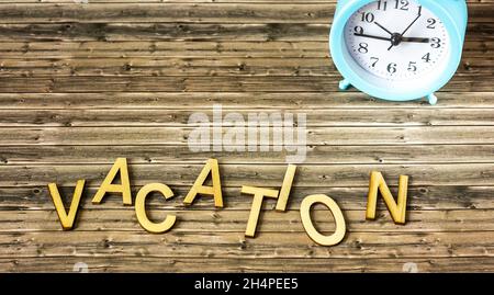 Wooden letters with the word VACATION on a wooden background with an alarm clock. Stock Photo