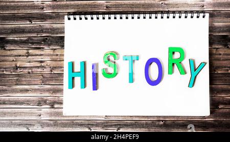 The word history is written in multicolored wooden letters on a white notebook. Wooden background. Stock Photo