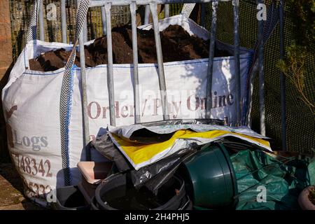 A jumble of things in the amateur smallholding garden. Compost store in disused log bag and various flower pots and empty plastic sacks Stock Photo