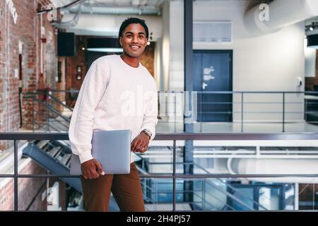 Happy young businessman smiling in a modern office. Confident young businessman looking at the camera while leaning against metal railings. businessma Stock Photo