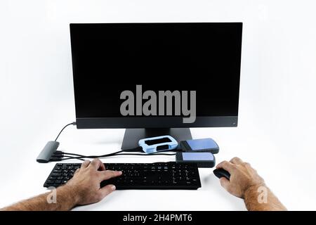 a person works on a computer by pressing the keyboard and holding a mouse on a white background.Monoblock with external hard drives. Stock Photo