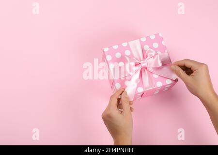 Female hands and gift box with bow on pink background Stock Photo