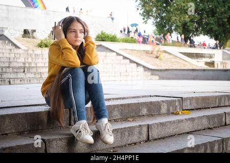 A sad teenage girl sits on the stairs and covers her head with her hands Stock Photo