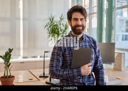 Smiling businessman leaning on his desk holding a digital tablet Stock Photo