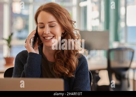 Smiling businesswoman talking on her phone at her office desk Stock Photo