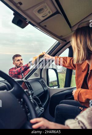 man cleaning motorhome windshield while woman pointing stain Stock Photo