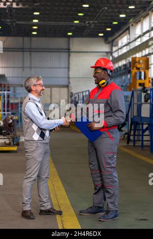 Smiling Multiracial Industrial Co-Workers Standing In A Factory And Talking Beside Next To Production Line. Stock Photo