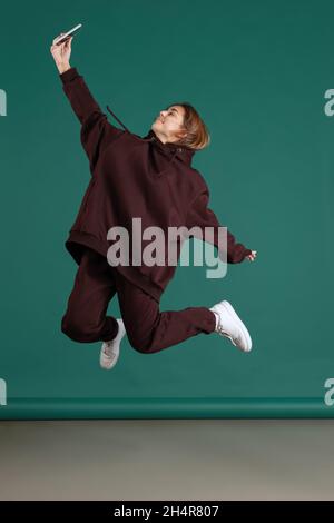 Full-length portrait of young beuatiful girl, student in brown sportive suit isolated on green vintage studio backgroud. Stock Photo