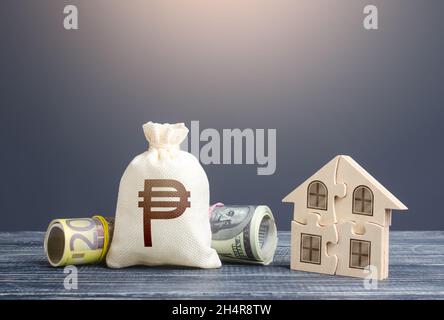 Philippine peso money bag and puzzle house. State social programs. Housing cooperative membership. Property valuation. Mortgage loan on purchase, buil Stock Photo