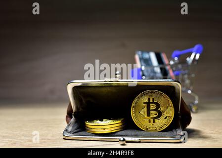 Bitcoins in the wallet. Gold crypto coins in a retro wallet with a shopping basket and a plastic card for purchasing goods. BTC mining and investing c Stock Photo