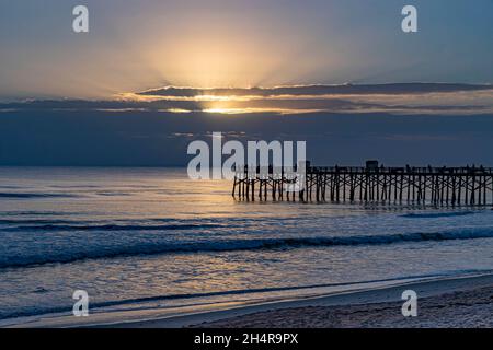 Sunbeams breaking through dark storm clouds on the horizon over the Flagler Beach Fishing Pier in Florida. Stock Photo