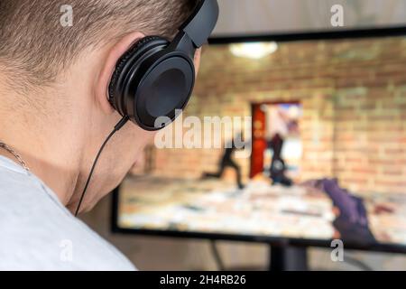 Rear view of a young man with headphones playing a video game on a computer at home Stock Photo