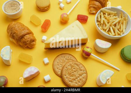 Unhealthy foods. French croissant, candy on a stick, jelly candies, marshmallows, cookies and macarons on a yellow bright background Stock Photo
