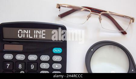 Online text on a calculator, near glasses and a magnifier on a white background Stock Photo