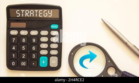 Magnifying glass on a color pie chart, calculator with the text Strategy on paper, pen, - concept of business, banking, finance and investment Stock Photo