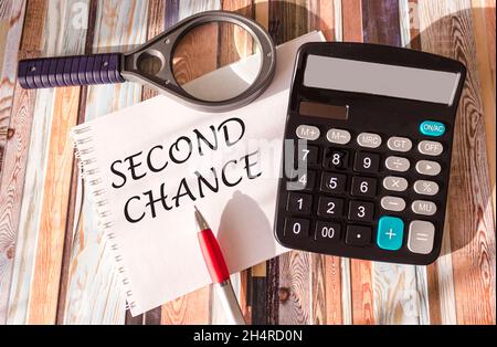 The text SECOND CHANCE is written on a notebook, near a calculator, a magnifier and a pen. Business concept Stock Photo