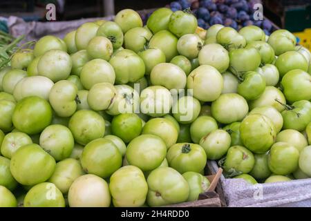 Close-up of a pile of green tomatoes of different sizes in a wooden box on the market Stock Photo