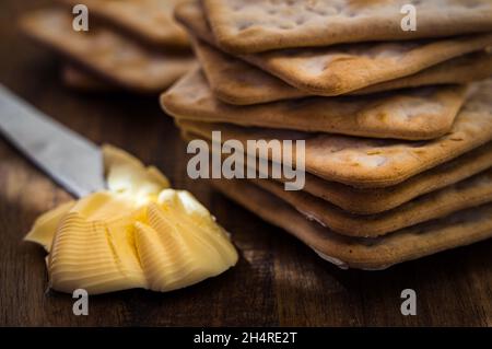 Tasty Cream Crackers on a wooden platter with butter ready to be spread Stock Photo