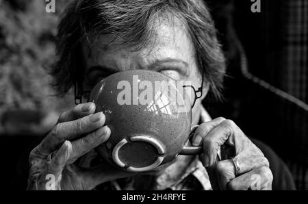 Elderly woman who has Essential Tremor using both hands drinking from a large cup or mug Stock Photo