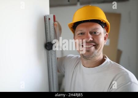 Portrait of cheerful male worker wearing protective yellow helmet checking level. Renovation in apartment. Professional carpenter. Accurate measuremen Stock Photo