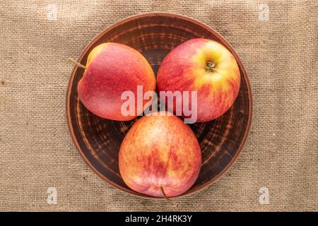 Three organic red apples with a clay dish on sacking, close-up, top view. Stock Photo