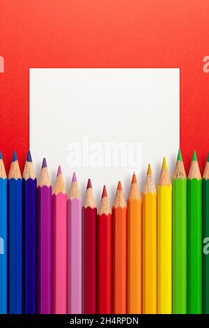 Creative layout made of color pencils on red paper background with white paper card note. Flat lay. Education concept. Stock Photo