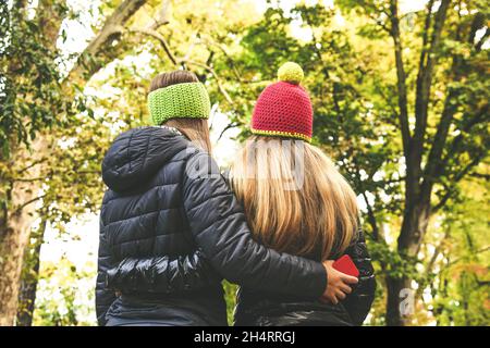 View from the back of two girls in the park. Teen walking outdoor in the forest. Young student woman enjoying free time in nature. Women embraced in a Stock Photo