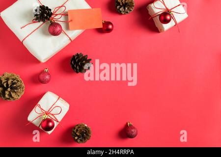 New Year's gifts are wrapped in craft paper and tied with a red jgut, lie among the balls and cones on a red background. Handmade packaging. Top view. Stock Photo