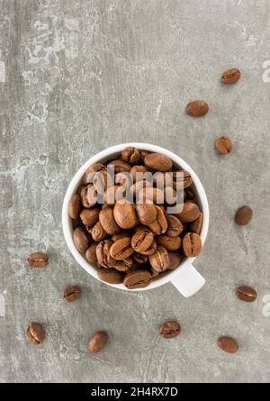 Whole medium roasted coffee beans in white cup over beautiful dark gray texture background with copy space. Top view. Stock Photo