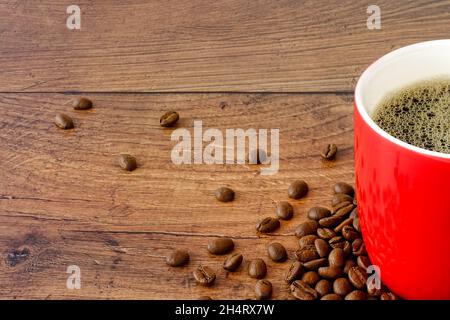 Close-up of a red coffee mug filled with coffee and coffee beans on a brown wood background with copy space. Straight on view. Stock Photo