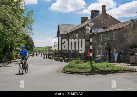 Cycling Yorkshire, view in summer of a man cycling past the historic Buck Inn in the centre of the scenic Yorkshire Dales village of Malham, England Stock Photo