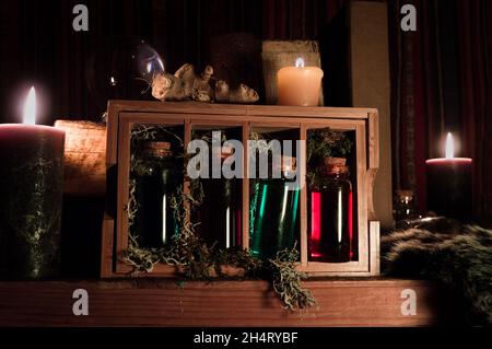 A dark scene with magical attributes focused on a wooden box with glass bottles filled with blue and red liquid. Stock Photo