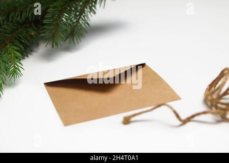 Craft eco envelope on white background. Christmas holiday concept. Letter to Santa Claus. Green natural background, fir tree branches. Simple rope. Stock Photo