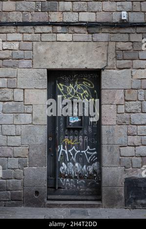BARCELONA, SPAIN - Jan 12, 2021: A vertical closeup of a black metal door with graffiti on a stone facade Stock Photo