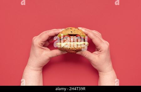 Top view with woman's hands holding a small vegan burger. Healthy food, a homemade cheeseburger with rye bread buns and soy meat patty. Stock Photo