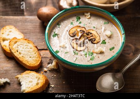 Homemade creamy mushroom soup with sliced mushrooms topping in an old bowl and bread toast on a rustic wooden table Stock Photo