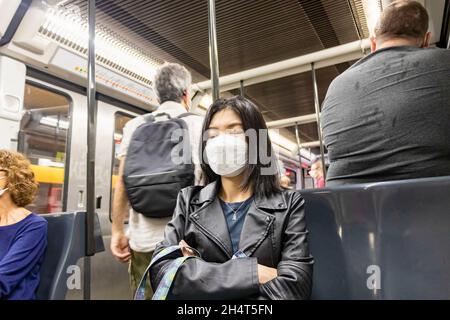 Barcelona, Spain - September 21, 2021: Exhausted asiatic woman take a nap on the train during her way to home, wearing protective face mask due to cor