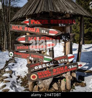 Touristic information signs under a wooden roof, on the way to Zygmuntowka mountain shelter. Snowy winter day. Owl Mountains, Sudetes, Poland. Stock Photo