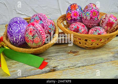 Still life with Easter eggs. Decorated Easter eggs lay in a wicker basket on a white wooden background. Easter eggs, decorated with traditional folk Stock Photo