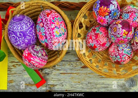 Still life with Easter eggs. Decorated Easter eggs lay in a wicker basket on a white wooden background, top view. Easter eggs, decorated with Stock Photo