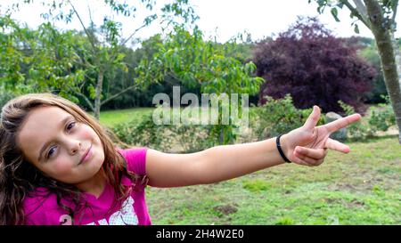 girl looking at the camera with her head down and her opposite arm stretched out showing three fingers of one hand