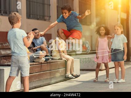 Energetic kids playing and skipping on elastic jumping rope in yard Stock Photo