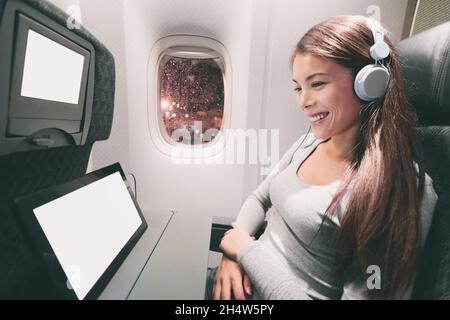 Passenger in airplane using tablet computer. Woman in plane cabin using smart device listening to music on headphones. Banner panorama travel people Stock Photo